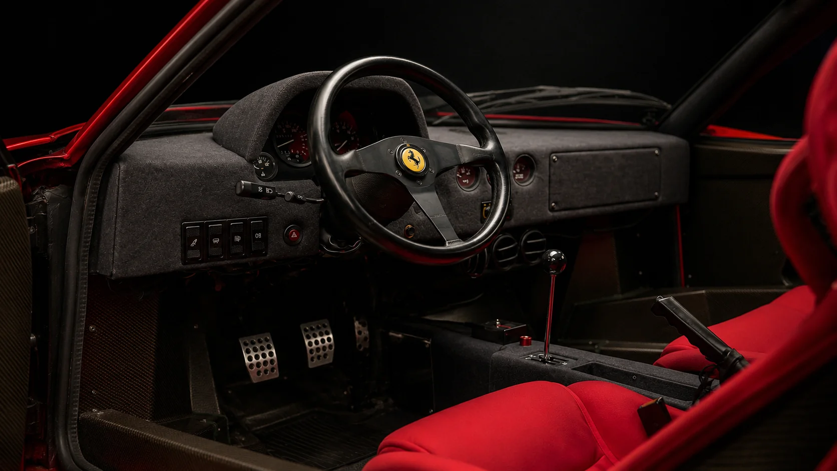 The spartan cabin of a Ferrari F40 with red cloth racing seats and a gated shifter